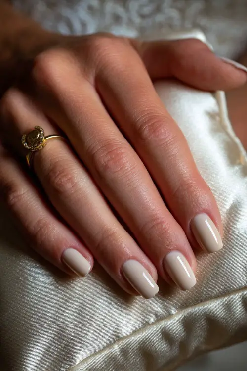 Soft shot of bride’s hand on silk pillow, acrylic ballerina nails in soft beige with matte finish and a tiny gold charm on the ring finger 