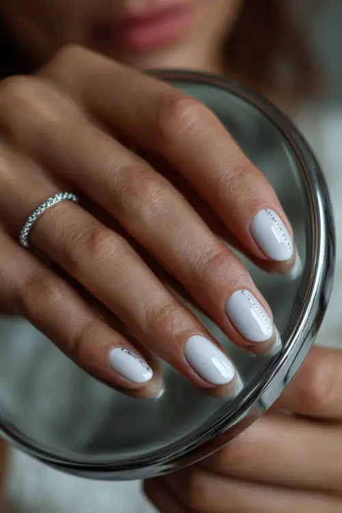 Soft touch of bride’s hand on a mirror, showcasing rounded nails with matte white finish and delicate rhinestone line art
