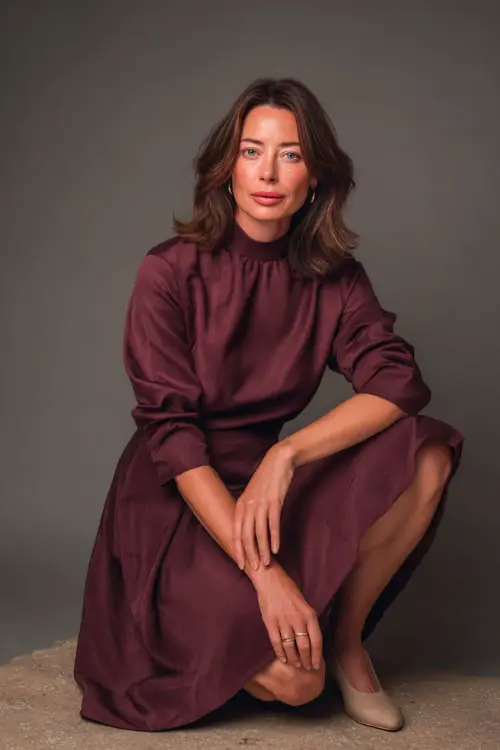 Elegant mature woman in a deep burgundy A-line dress with a high neckline and elbow-length sleeves, styled with low block heels and minimal jewelry