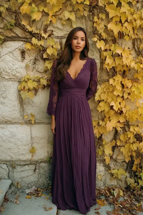 Elegant woman in a plum maxi dress with lace sleeves and scalloped neckline, standing beside a stone wall covered in golden ivy and dried fall vines 