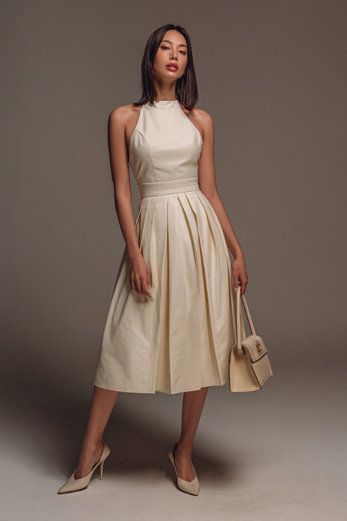 Full-body image of a woman in a sleeveless ivory midi dress with a pleated skirt, cinched waistline, paired with classic slingback heels and a structured handbag