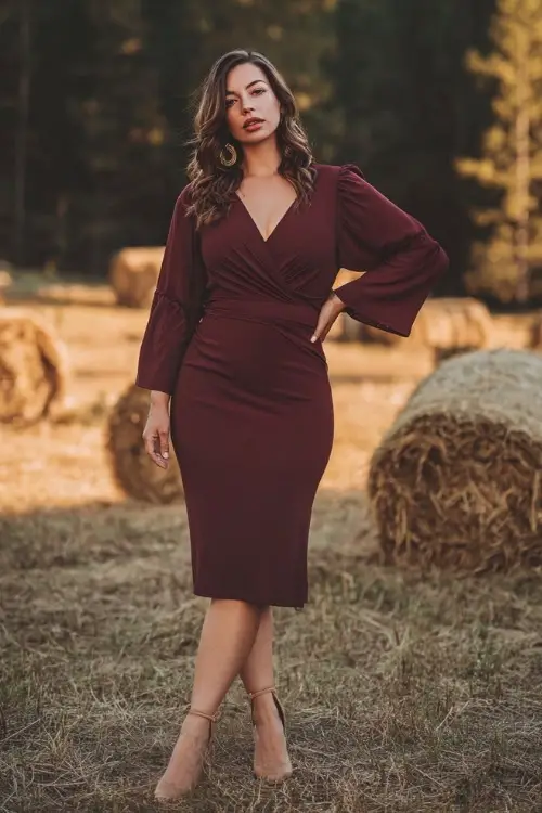 Full body of a curvy woman in a burgundy wrap midi dress with long flutter sleeves and a V-neckline