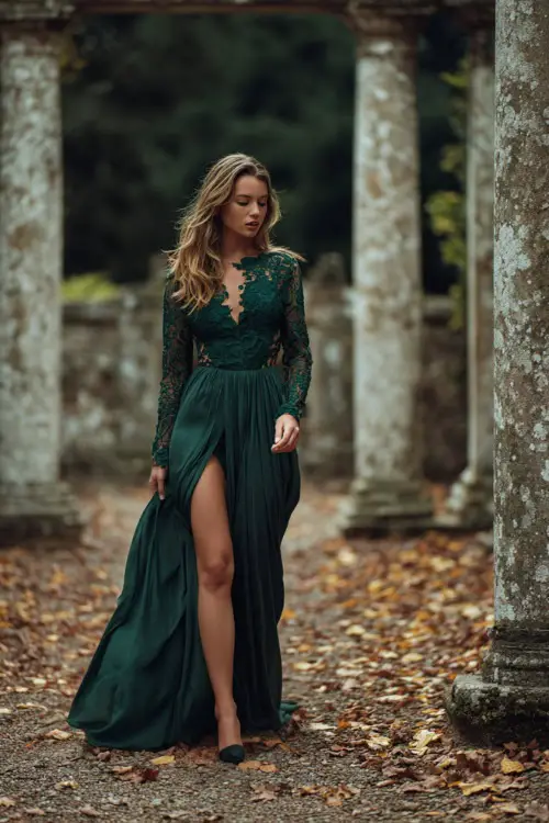 Full body of a woman in a dark forest green gown with lace sleeves and dramatic slit, walking across a courtyard wedding venue with falling leaves and stone pillars 