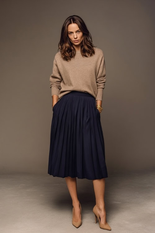 Full-body portrait of a woman in a navy pleated midi skirt with a tucked-in taupe sweater, tan heels, and minimal accessories, soft studio light
