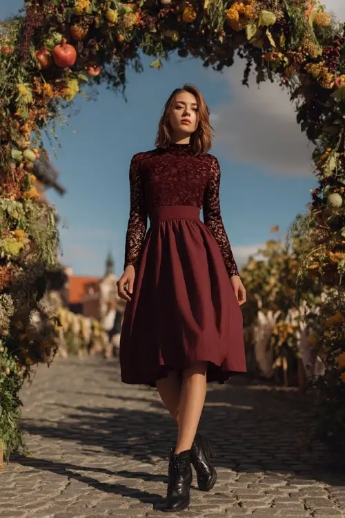 Mature woman in a wine-colored A-line midi dress with lace sleeves and black ankle boots, standing on a cobblestone path near a fall-themed wedding arch