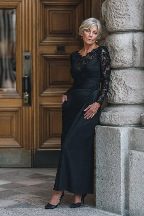 Sophisticated older woman in a black long-sleeve gown with lace detailing and classic heels, posing at the entrance of a grand fall wedding venue 