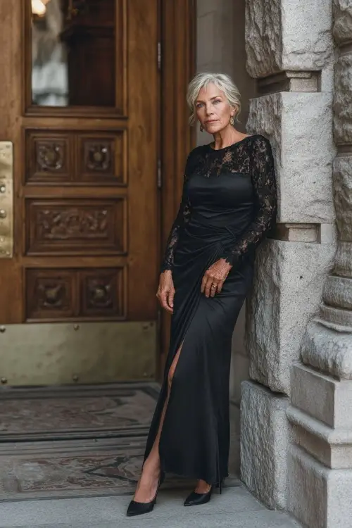 Sophisticated older woman in a black long-sleeve gown with lace detailing and classic heels, posing at the entrance of a grand fall wedding venue 