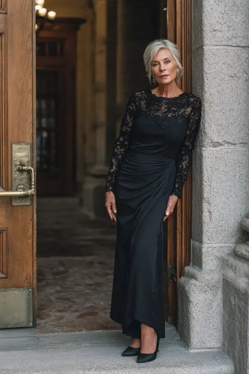 Sophisticated older woman in a black long-sleeve gown with lace detailing and classic heels, posing at the entrance of a grand fall wedding venue