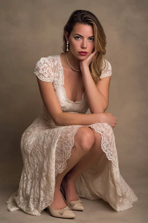 Woman in a floor-length cream A-line dress with lace overlay and cap sleeves, styled with pearl drop earrings and ivory pumps, posed gracefully in a neutral-toned studio