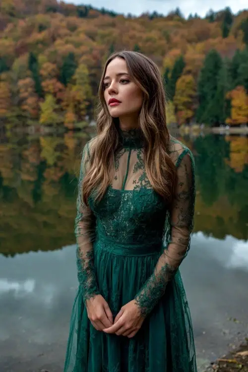 Woman in a forest green midi dress with lace overlay and long sheer sleeves, standing at a lakeside wedding with fall foliage reflections, full body visible 