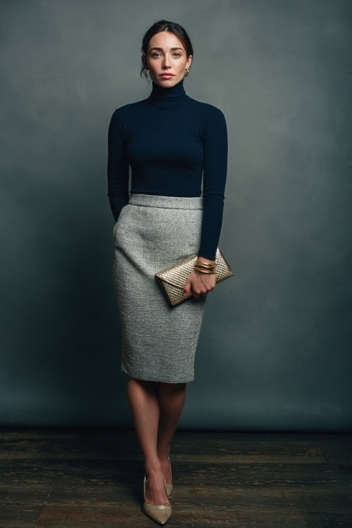 Woman in a gray tweed pencil skirt with a navy turtleneck and low heels, styled with a vintage clutch and subtle gold jewelry, posed in a simple studio