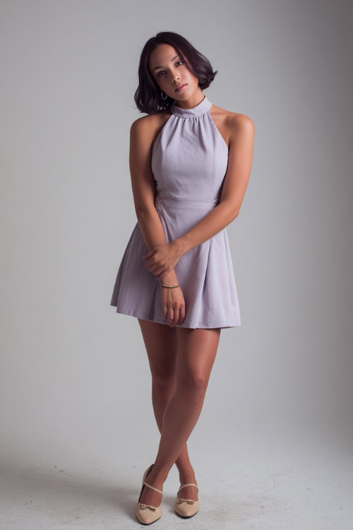 Woman in a pale lavender sleeveless dress with a vintage silhouette, styled with simple jewelry and beige Mary Janes, posed full-body in a bright