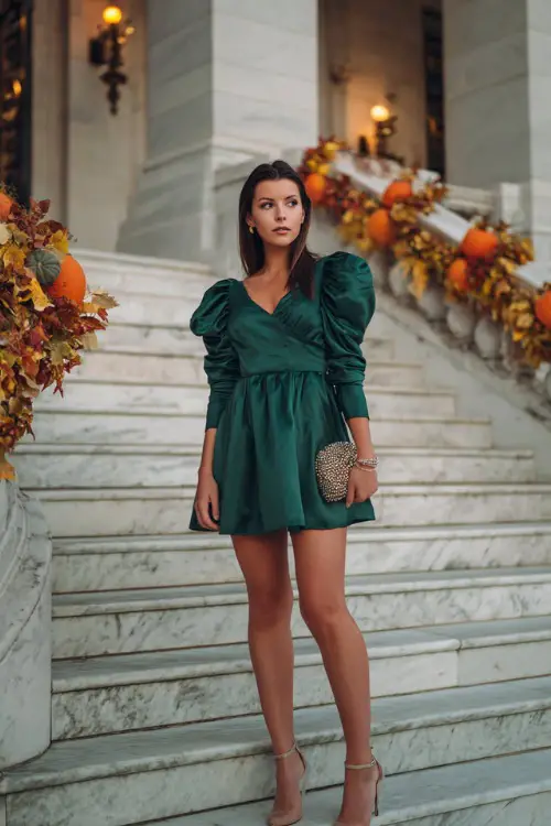 A woman in a short emerald green A-line dress with puff sleeves, styled with a jeweled clutch and ankle-strap heels