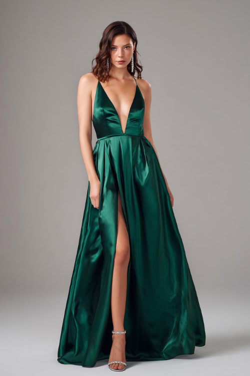 A woman wears a deep emerald green satin A-line gown with a plunging neckline, paired with crystal drop earrings and silver strappy heels for a black-tie fall wedding 