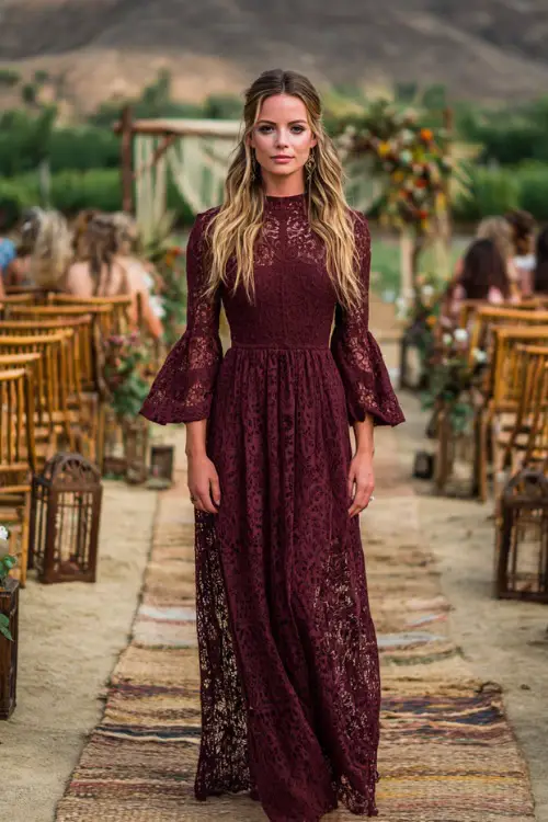 Woman in a deep burgundy crochet-lace boho maxi dress with bishop sleeves, barefoot on a woven rug aisle in an outdoor October wedding setting