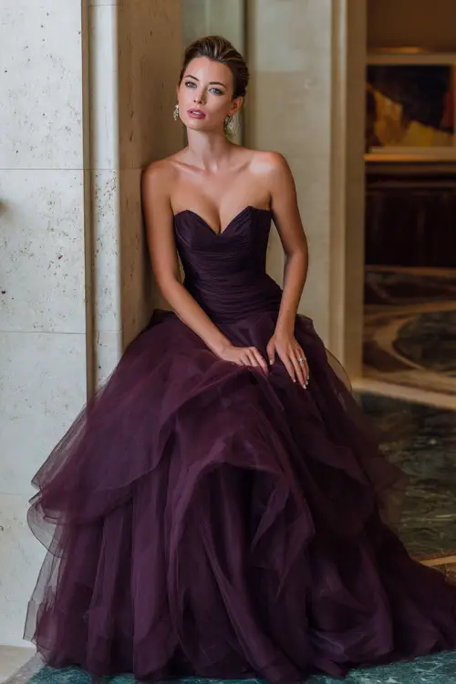 Woman in a deep plum strapless ball gown with layered tulle skirt and elegant updo, posing at a sophisticated October indoor wedding venue, full body 