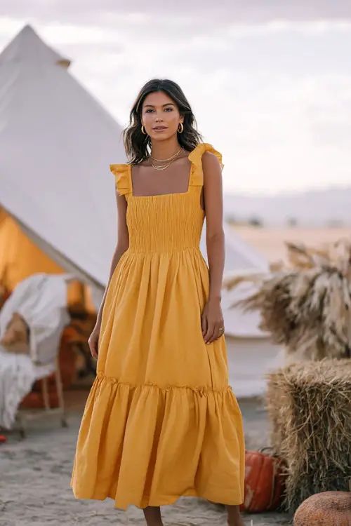 Woman in a marigold tiered midi dress with square neckline and smocked bodice, styled with block heels and delicate gold jewelry 