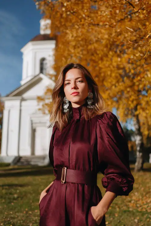 Woman in a maroon midi dress with puff sleeves and a belted waist, accessorized with statement earrings 