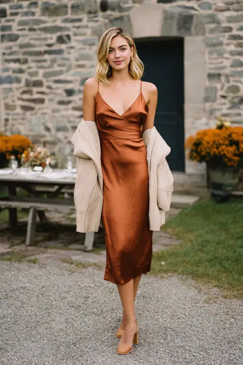 Woman wearing a copper satin midi slip dress with a light shawl draped over her shoulders, paired with block heels