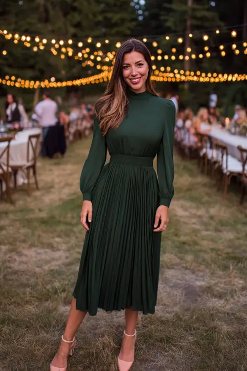 Woman wearing a forest green pleated midi dress with a high neckline and long sleeves, styled with ankle strap heels