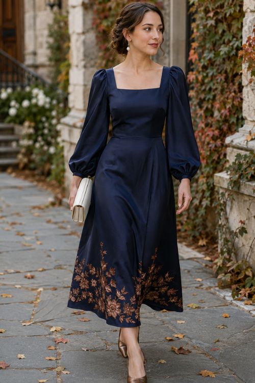 a woman wearing a navy satin midi dress with a sculpted square neckline, softly puffed sleeves, and copper floral embroidery along the hem