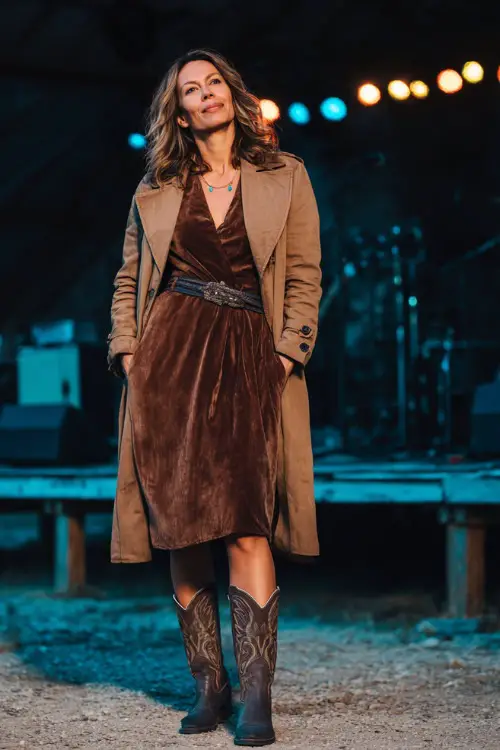 A woman over 40 styled in a velvet midi dress with a belted waist, paired with tall cowboy boots and a wool coat