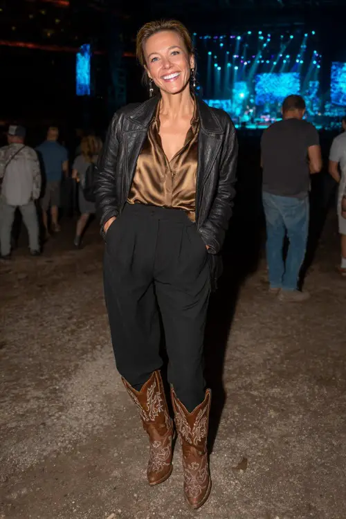 A woman over 40 in tailored black pants, satin blouse, cropped leather jacket, and embroidered cowboy boots