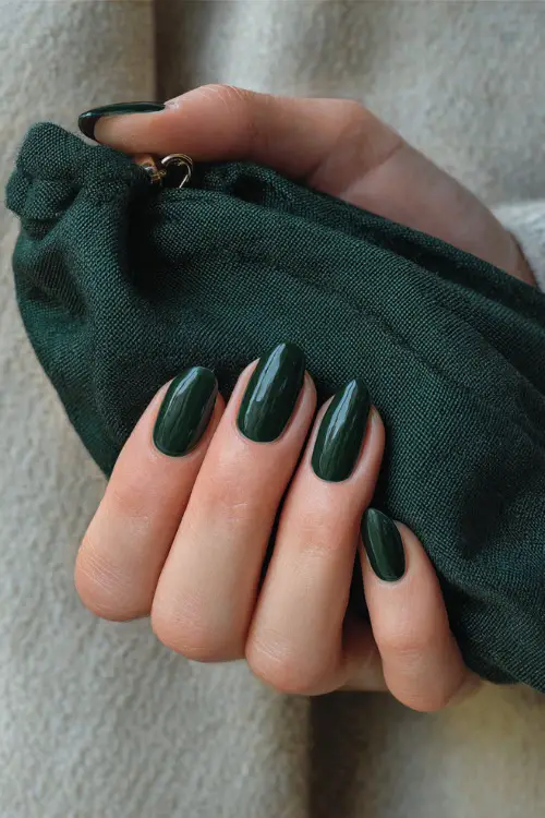Almond-shaped short nails painted in dark green glossy finish, bridesmaid’s hand holding a satin clutch bag 