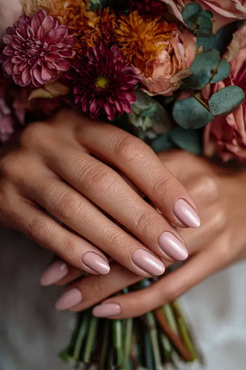 Bridesmaid’s hands with almond-shaped soft blush pink nails, holding a bouquet of autumn roses and dahlias 