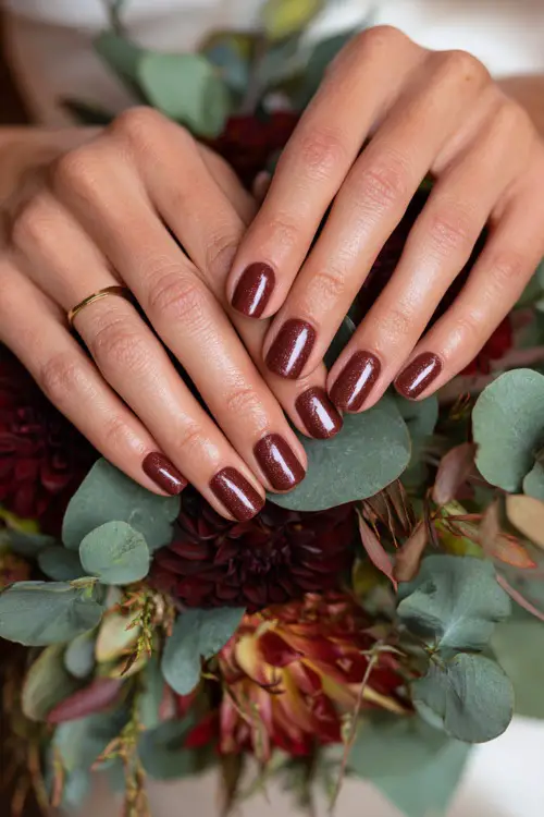 Burgundy nails with subtle copper glitter highlights, bride’s hands holding a fall bouquet of dahlias and eucalyptus