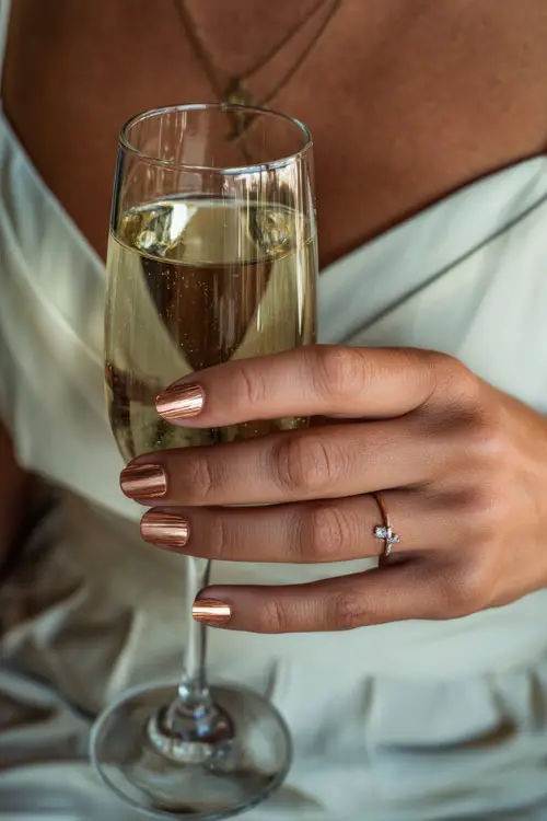 Cream-colored short nails with copper foil accents, bridesmaid holding a champagne glass during reception 
