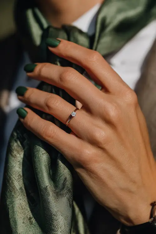 Dark green glossy nails with subtle shimmer, guest’s hand adjusting a silk scarf at an outdoor wedding 