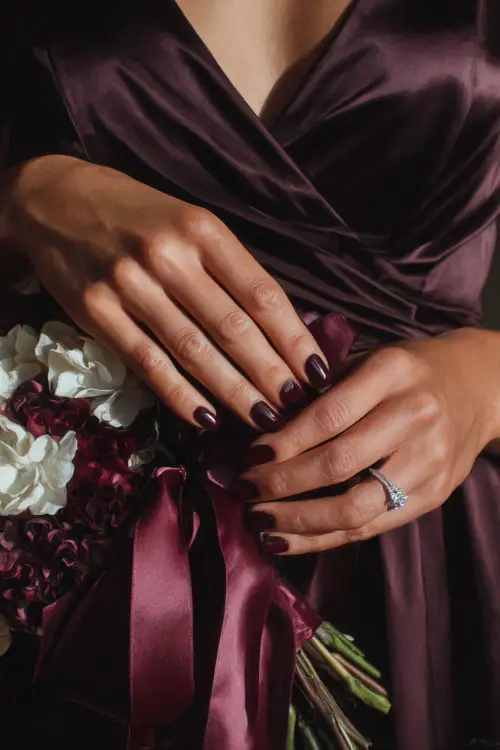 Dark plum glossy nails with rhinestone accents, bridesmaid’s hands adjusting a silk ribbon bouquet