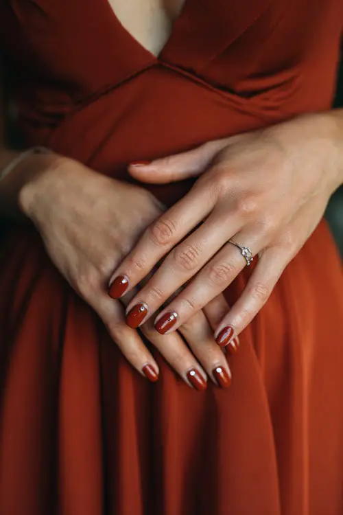 Dark rust matte nails with small rhinestone accents, bridesmaid’s hands placed over soft chiffon bridesmaid gown