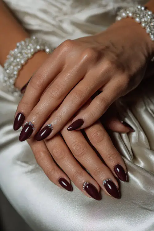 Deep burgundy chrome nails with rhinestone details, bride’s hands placed over satin bridal gloves