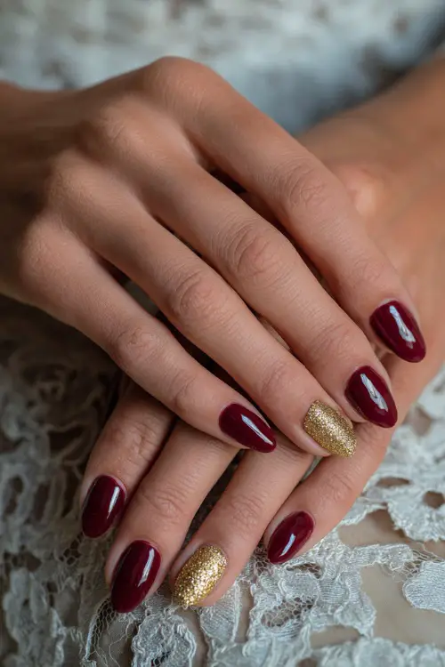 Elegant coffin-shaped burgundy nails with gold glitter tips, bride’s hands resting on lace wedding gown fabric 