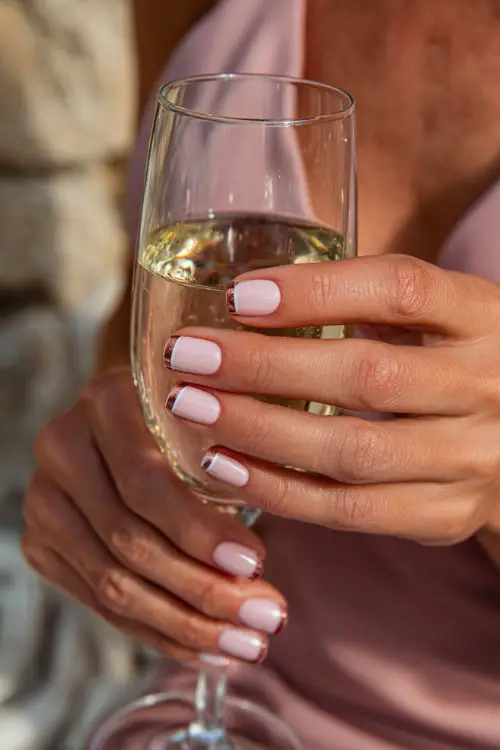 French manicure with blush pink base and rose gold tips, bridesmaid holding a wedding toast glass 