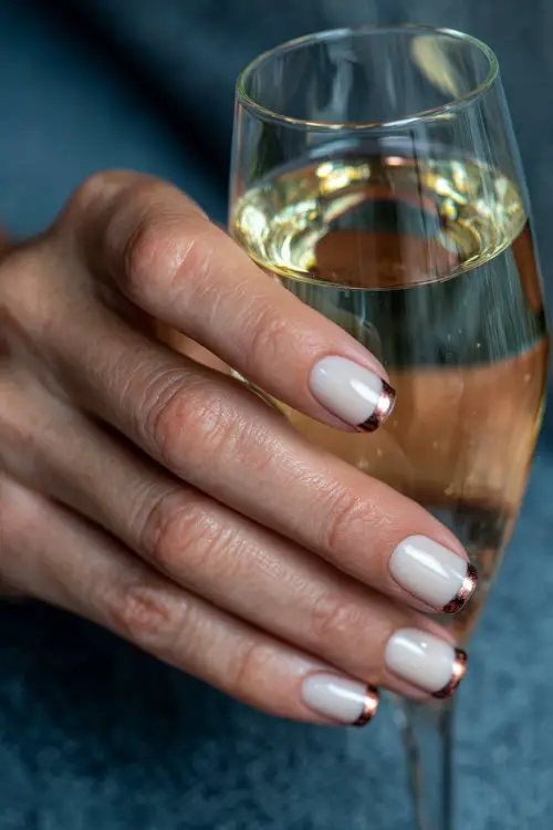 French manicure with cream base and copper metallic tips, guest holding a champagne flute 