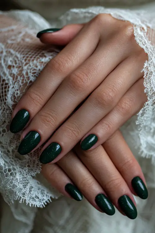 Glossy deep green nails with fine glitter accents, bride’s hands placed over lace bridal gloves 
