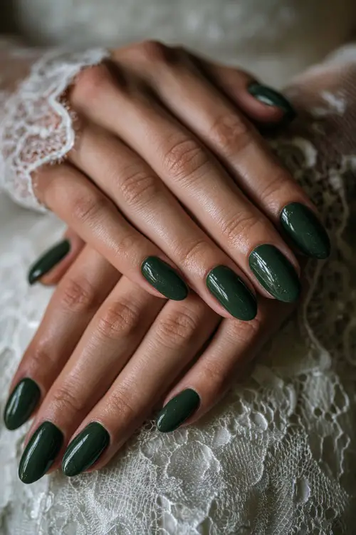 Glossy deep green nails with fine glitter accents, bride’s hands placed over lace bridal gloves 