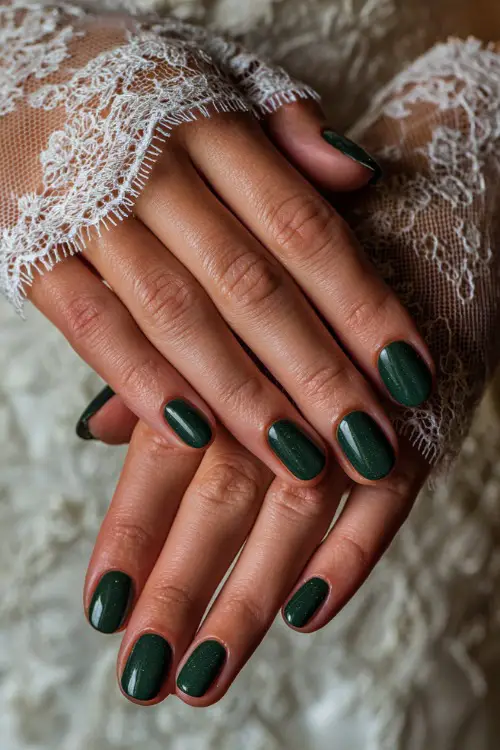 Glossy deep green nails with fine glitter accents, bride’s hands placed over lace bridal gloves