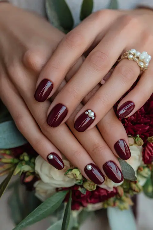 Glossy maroon nails with pearl-studded cuticle accents, bridesmaid’s hands holding a floral corsage