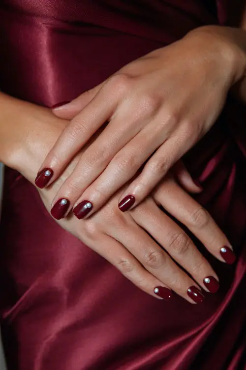 Glossy maroon nails with tiny pearl details, guest’s hands placed on an elegant satin dress