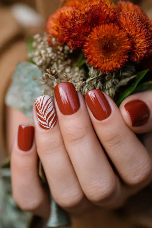 Glossy rust orange nails with hand-painted leaf designs, bridesmaid’s hand holding a floral corsage in autumn wedding setting 