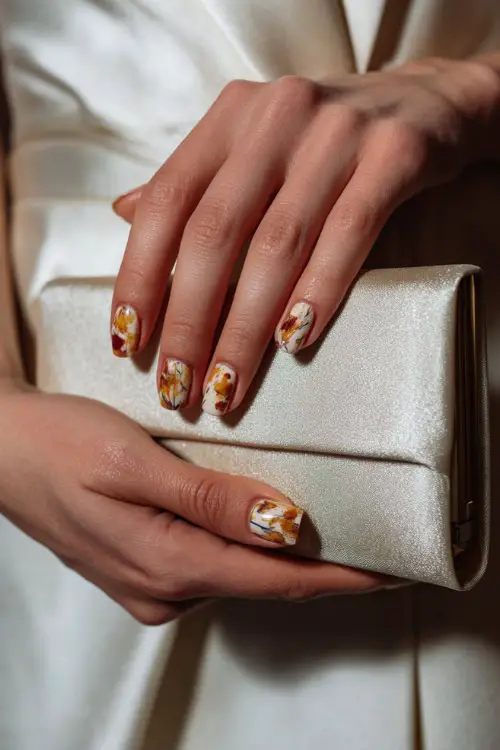 Ivory nails with hand-painted floral patterns in warm fall tones, bride holding a satin bridal clutch