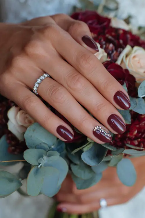 Maroon nails with jeweled cuticle accents, bride’s hands holding a fall bouquet of roses and eucalyptus 