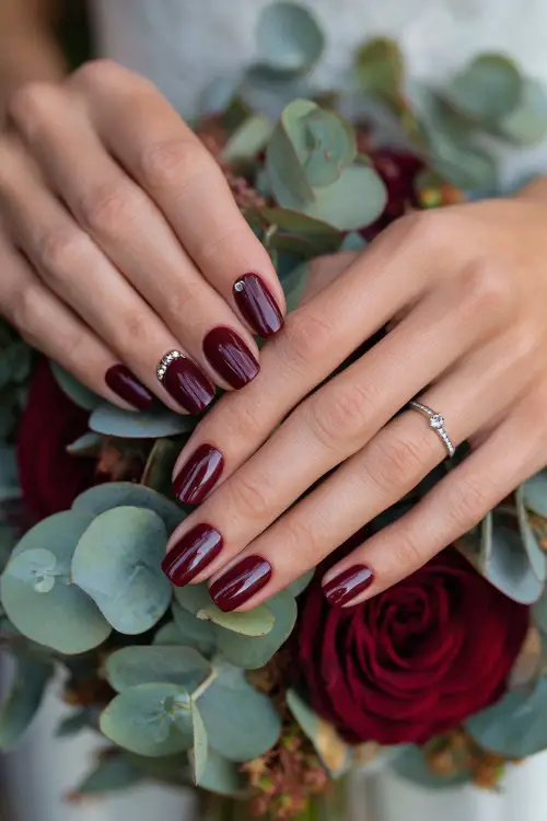 Maroon nails with jeweled cuticle accents, bride’s hands holding a fall bouquet of roses and eucalyptus