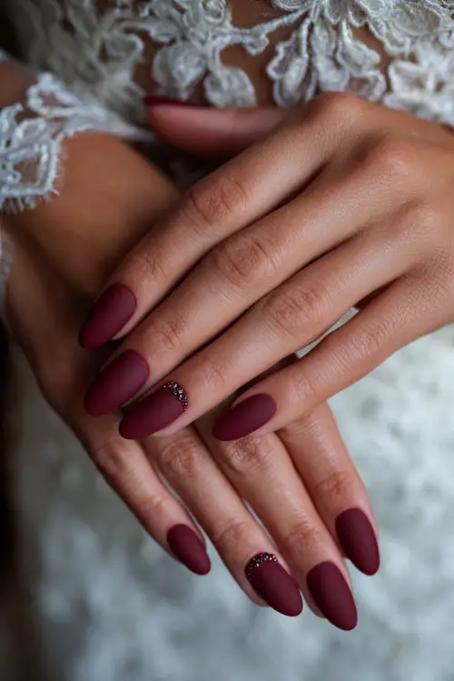 Matte burgundy nails with jeweled cuticle accents, bride’s hands resting on her wedding dress with lace embroidery 