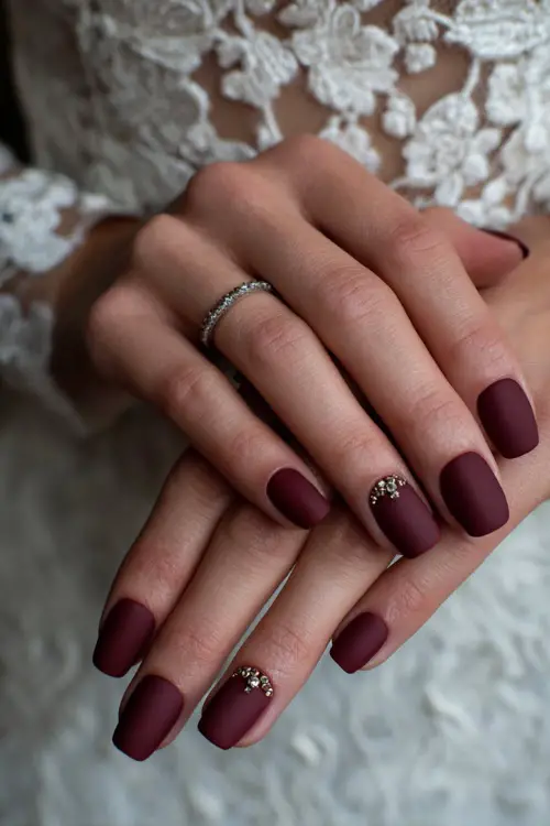 Matte burgundy nails with jeweled cuticle accents, bride’s hands resting on her wedding dress with lace embroidery