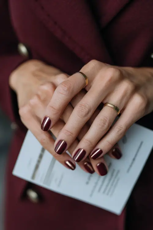 Matte burgundy nails with minimal gold line art, guest holding a wedding program 